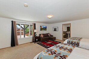 A hotel room with a large window, a sofa, a bed with patterned bedding, a rug, and a mirror.