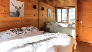 Habitación de cabaña de madera con cama, espejo y ventana con vistas nevadas.