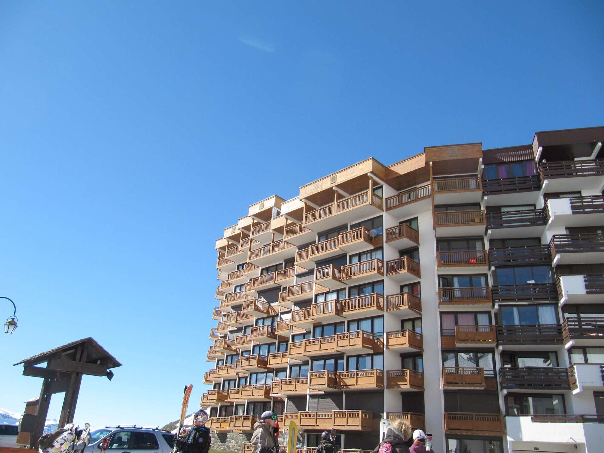 A multi-story hotel with balconies, a ski lift, and a mountain backdrop.