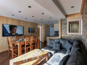 A modern living room with a wooden dining table, a grey sofa, and a stone accent wall. - Val Thorens: Stunning apt for 8, close to slopes and shops (Val Thorens)
