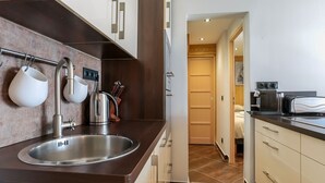 Una cocina moderna con un lavamanos de acero inoxidable, un hervidor y un tostador. Hay una encimera de madera y una puerta que da a otra habitación.