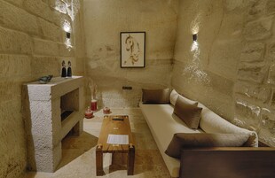 A stone-walled room with a wooden coffee table, a sofa, and a fireplace with decorative items.