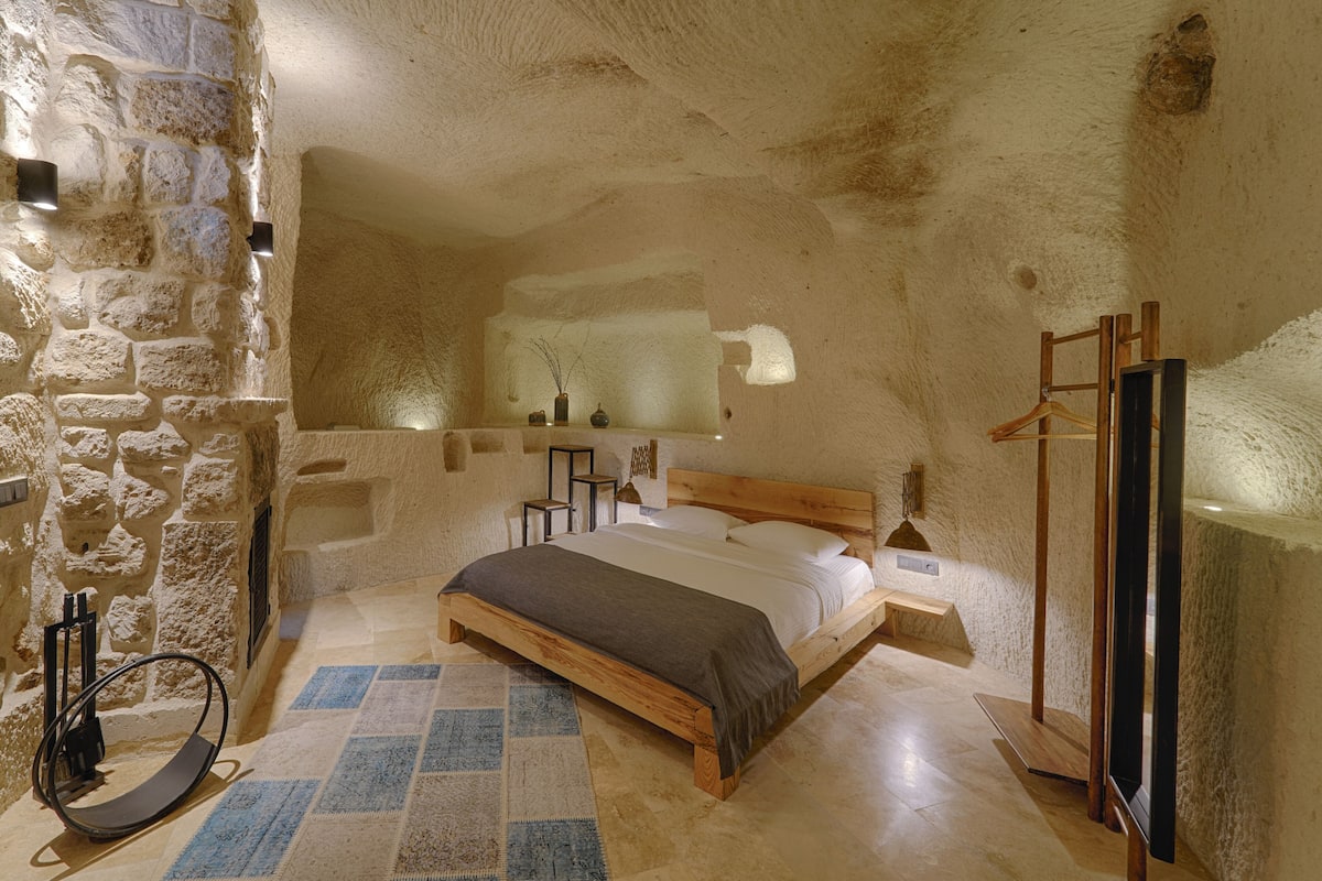 A bedroom with a stone wall, a wooden bed, a bench, and a mirror.