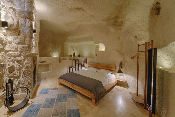Un dormitorio con pared de piedra, una cama de madera, un banco y un espejo.