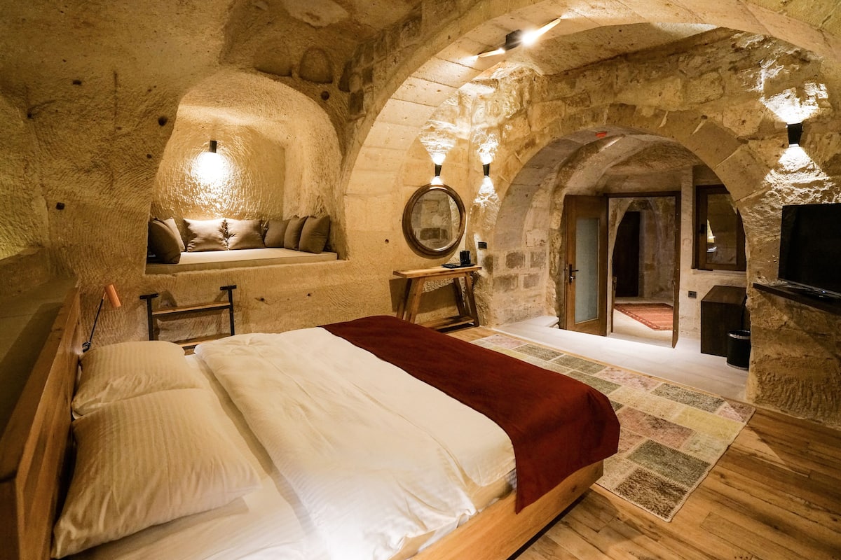A cozy, stone-walled bedroom with a wooden bed, a bench with cushions, and a mirror on the wall.