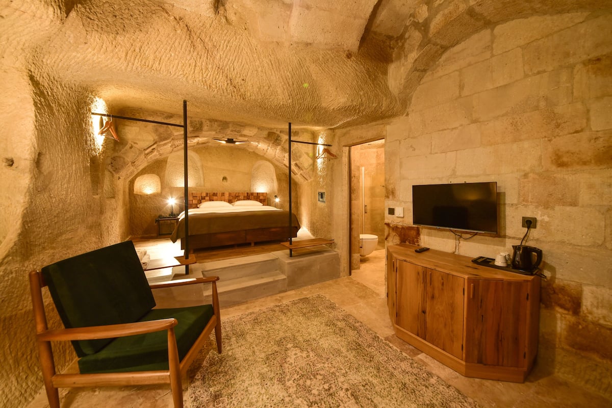 A cozy, stone-walled bedroom with a bed, a wooden cabinet, and a television.