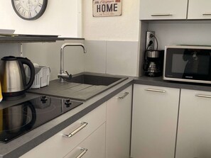 A modern kitchen with a built-in microwave, kettle, and a sink with a faucet. - Charming 1-Bedroom Apartment with Private Terrace Near Thau Lagoon (Balaruc-les-Bains)