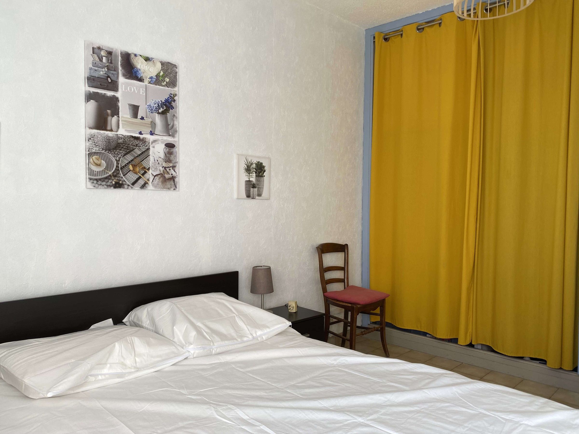 Un dormitorio con cama, una silla, una lámpara y una pared con cuadros.