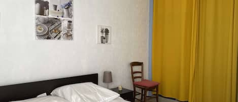 Un dormitorio con cama, una silla, una lámpara y una pared con cuadros.