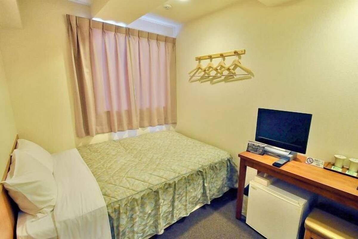 A small hotel room with a bed, a desk with a computer, a TV, and a mini-fridge.