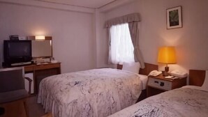 A hotel room with two beds, a desk with a television, a lamp, and a telephone.