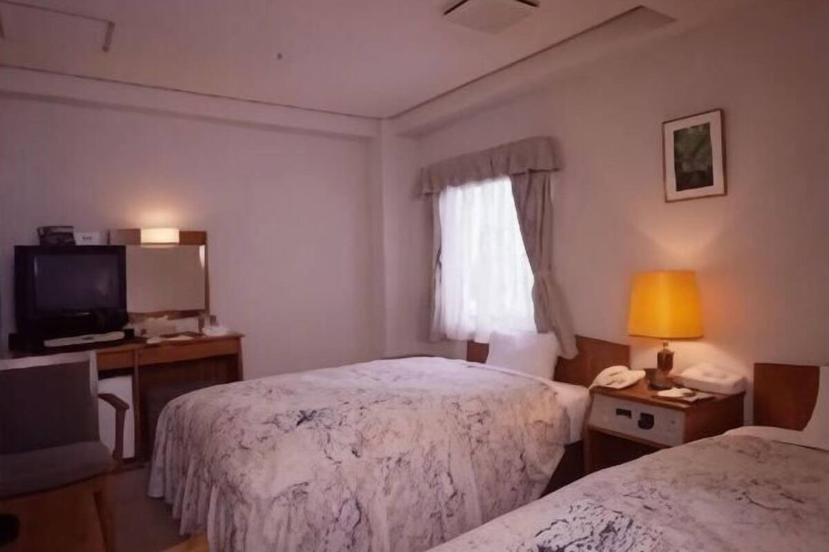 A hotel room with two beds, a desk with a television, a lamp, and a telephone.