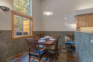 En matplats med ett träbord och stolar, en hängande lampa och ett fönster med utsikt över träd.