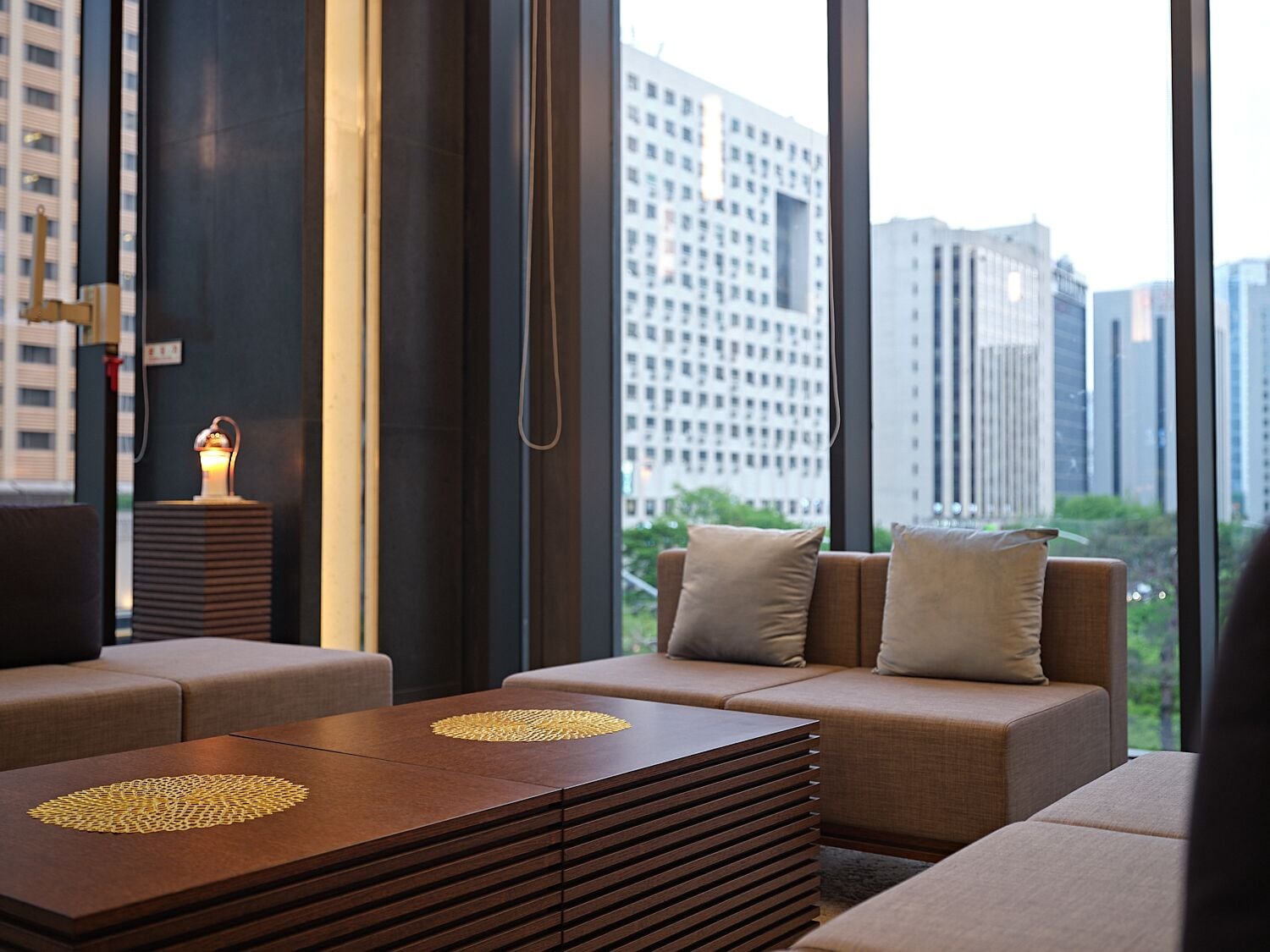 Una habitación de hotel moderna con un ventanal grande, un conjunto de sofá, una mesa de centro de madera y una lámpara.