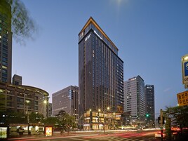 A modern hotel with a prominent corner entrance, multiple floors, and a well-lit facade.