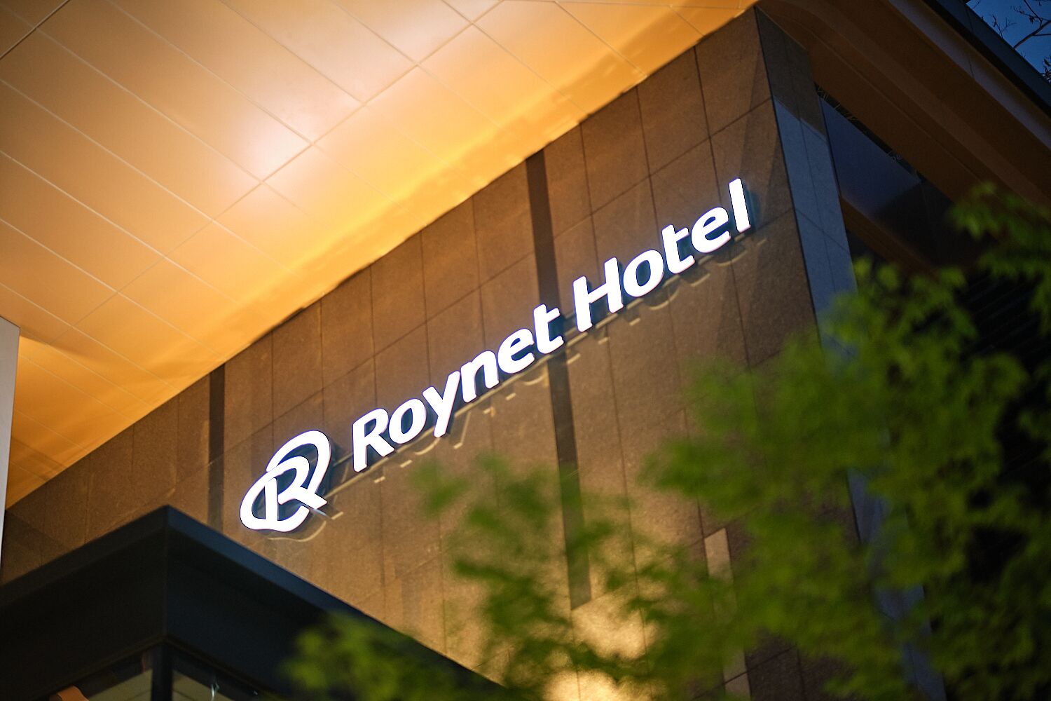 The exterior of the Roynet Hotel with its illuminated logo and modern architectural design.
