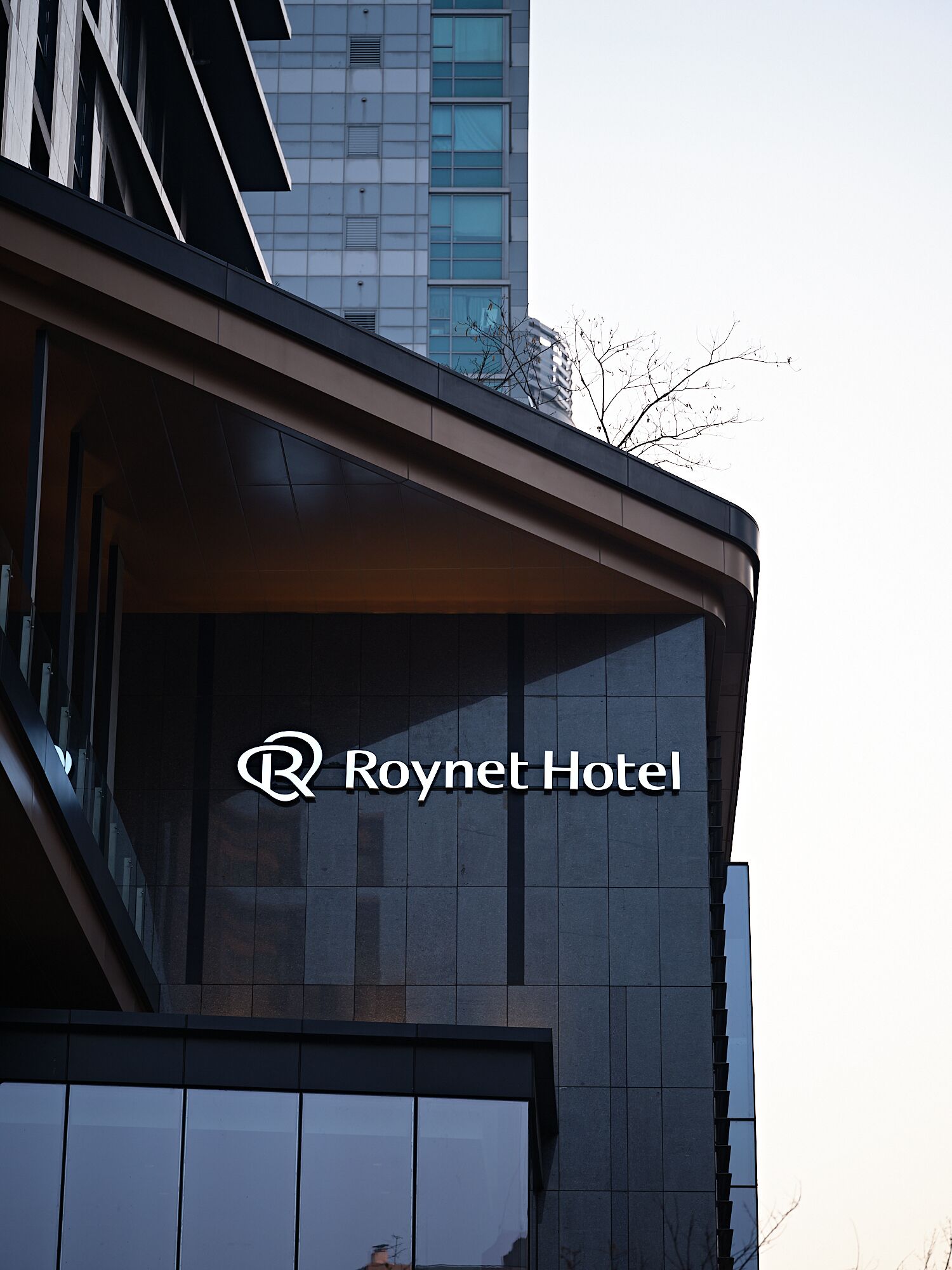 A modern hotel building with a prominent logo and a glass facade.
