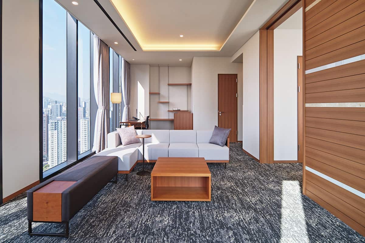 Une chambre d’hôtel moderne dotée d’une grande fenêtre donnant sur la ville, d’un canapé, d’une table basse et d’une armoire en bois.