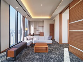 A modern hotel room with a large window offering a city view, a sofa, a coffee table, and a wooden wardrobe.