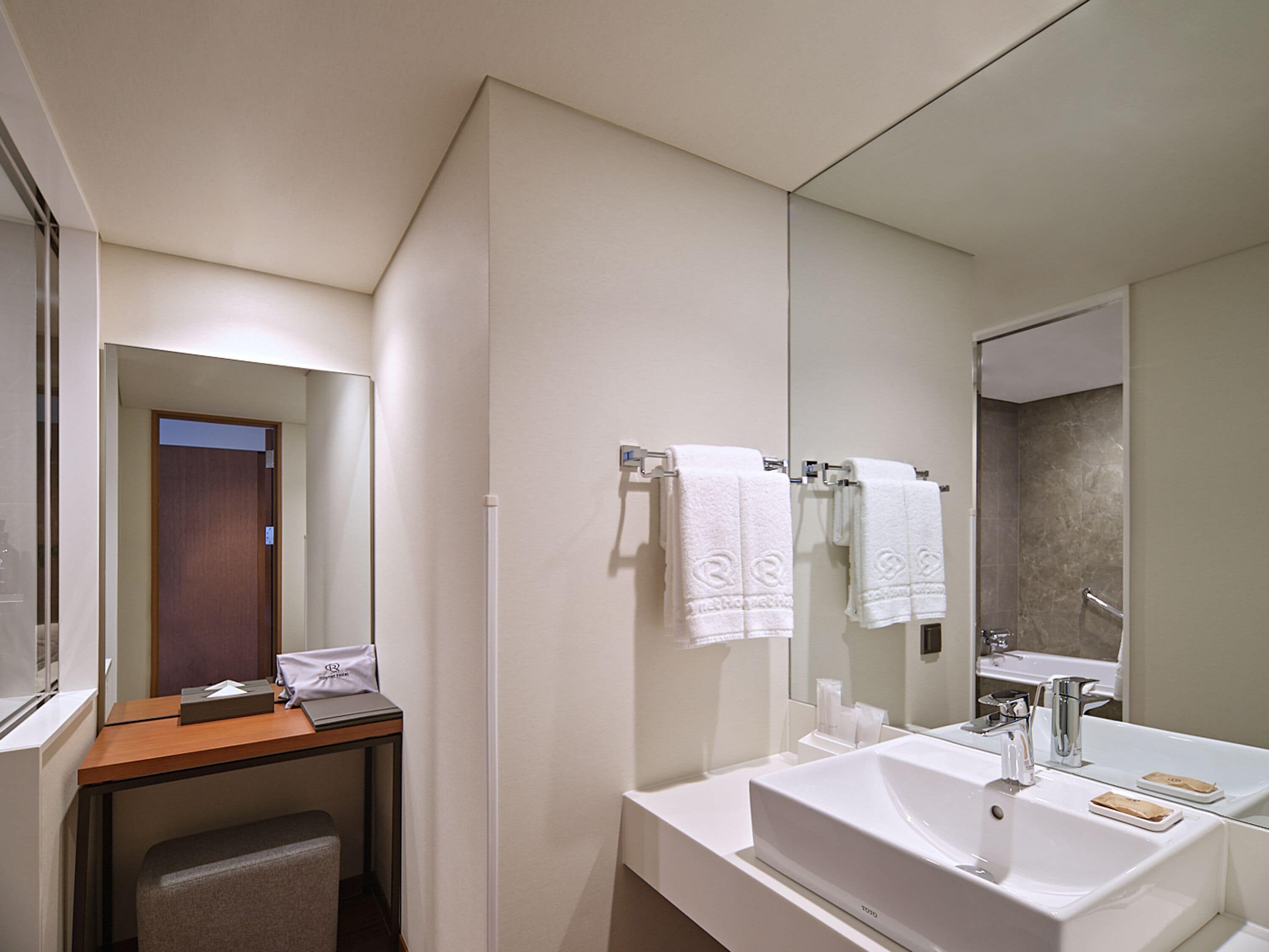 A modern bathroom with a large mirror, white sink, and towel rack.