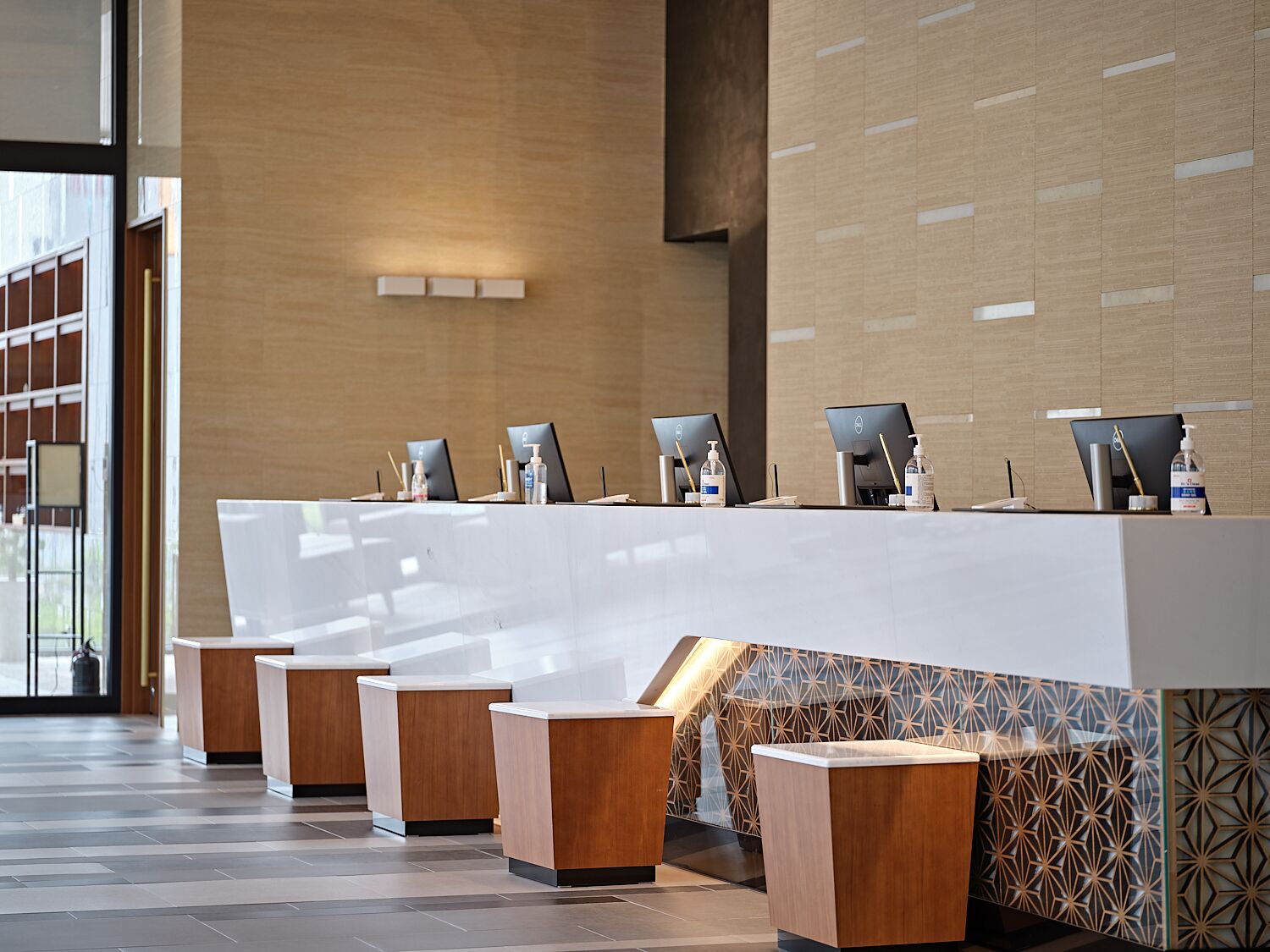 A modern reception desk area with multiple computer stations, each equipped with a monitor, keyboard, and a bottle of hand sanitizer.
