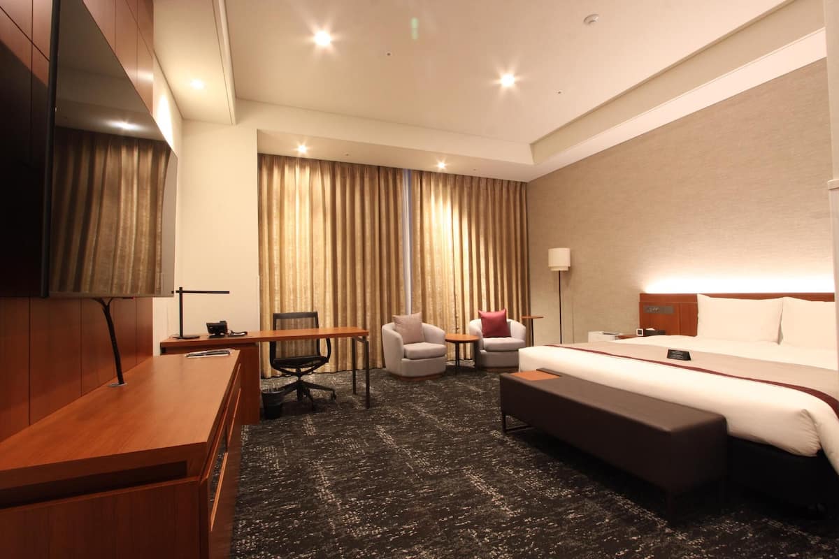 Une chambre d’hôtel avec un grand lit, un bureau, deux fauteuils, une petite table et un téléviseur.