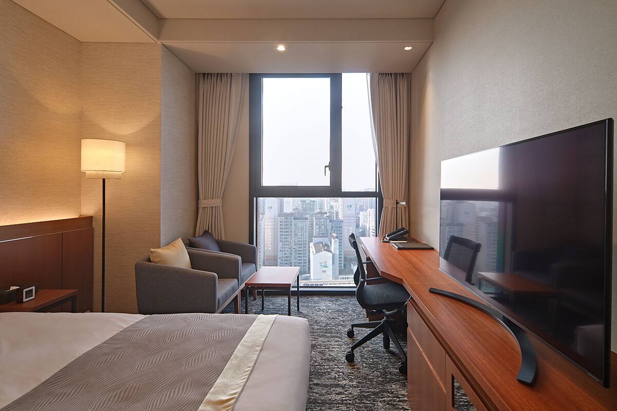 Une chambre d’hôtel avec un lit, un bureau, une chaise, une télévision et une vue sur la ville.