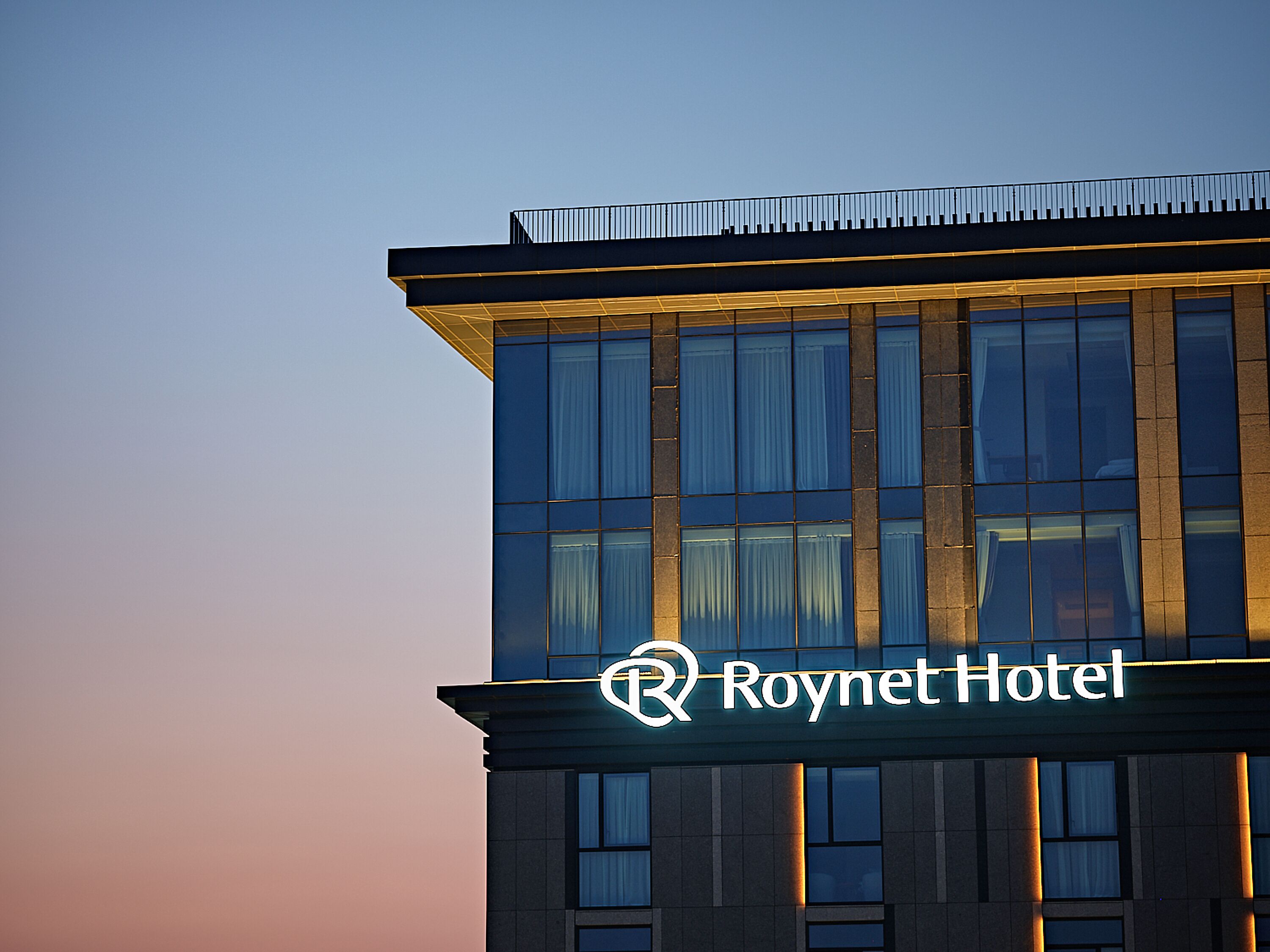 Un moderno edificio de hotel con un llamativo logotipo en forma de 'R' y la señalización 'Roynet Hotel'.