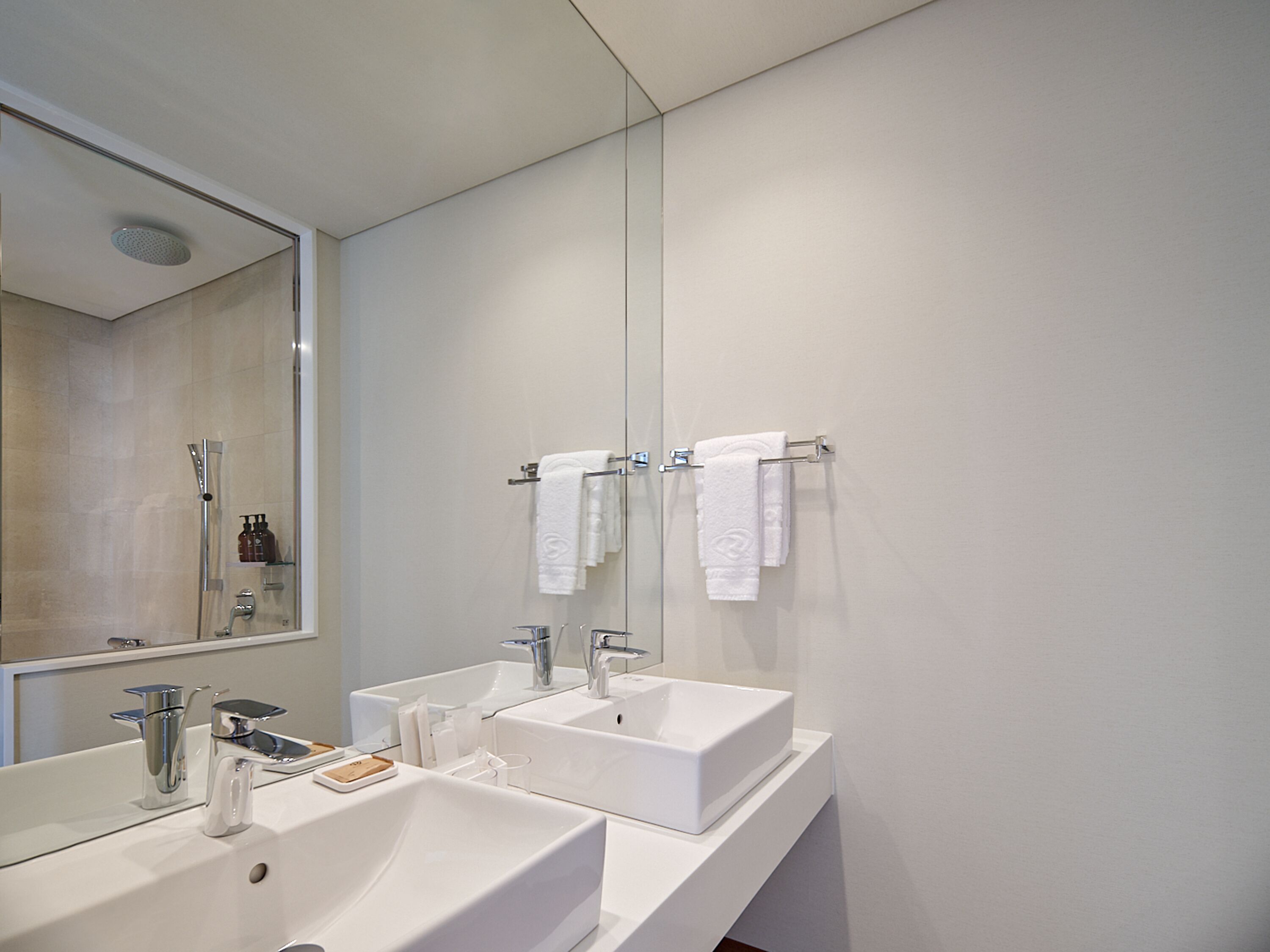 A modern bathroom with two sinks, a large mirror, and a shower.