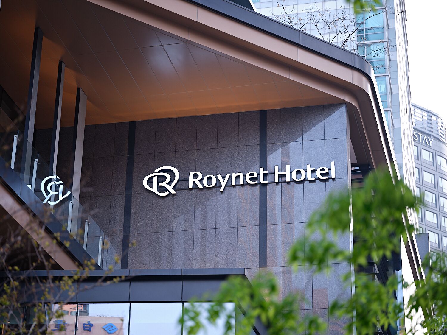 A modern hotel facade with the 'Roynet Hotel' sign prominently displayed.