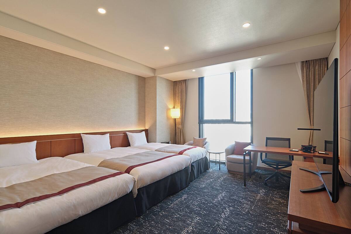 Une chambre d’hôtel avec deux lits, un bureau, une chaise et une grande fenêtre.