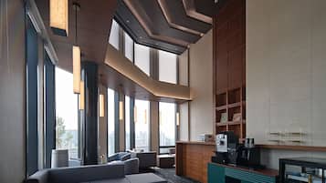 A modern lounge area with seating, a coffee station, and a view of the city.