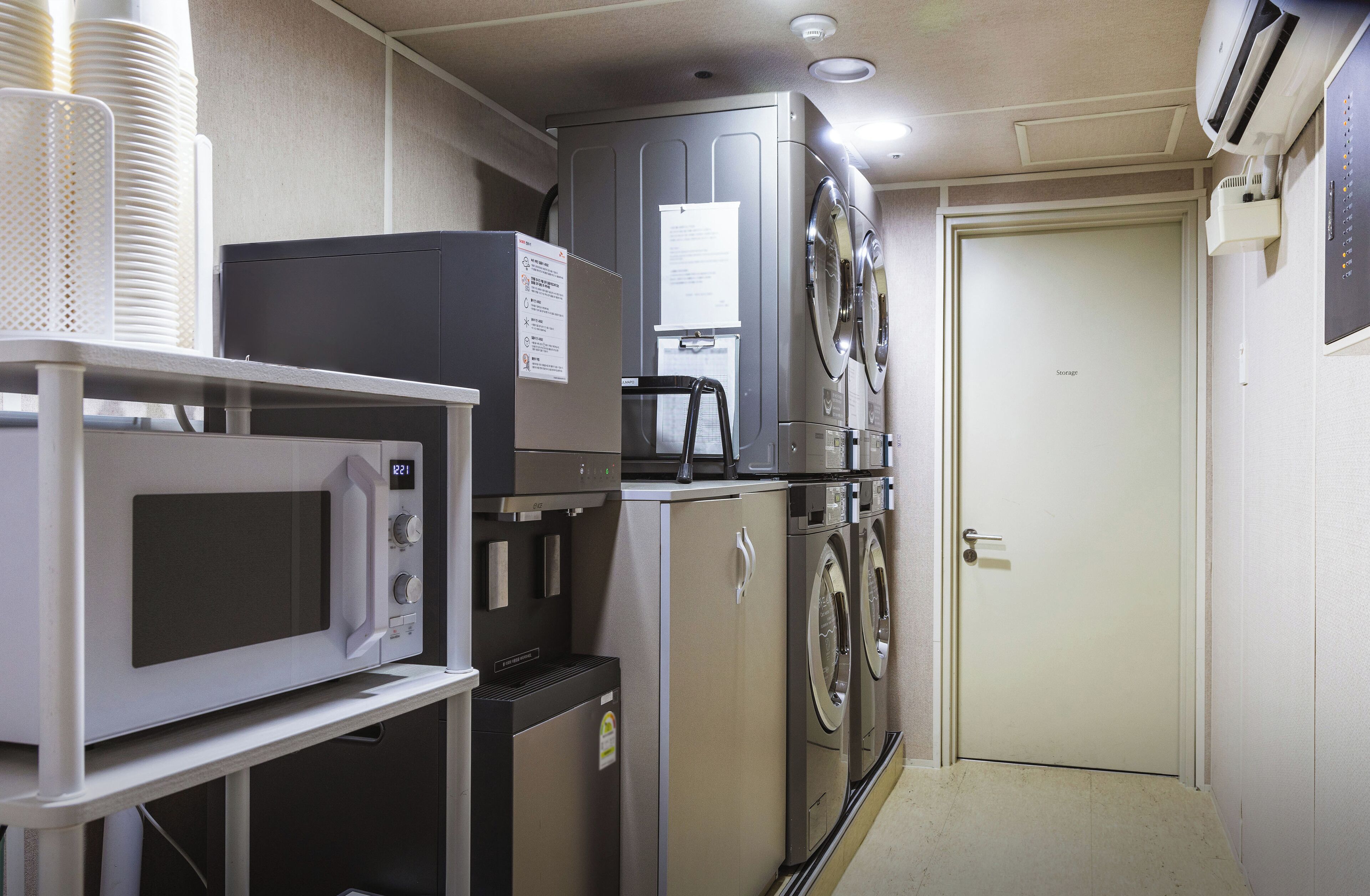 Habitación de hotel compacta con microondas, refrigerador y tazas blancas apiladas sobre una mesa.