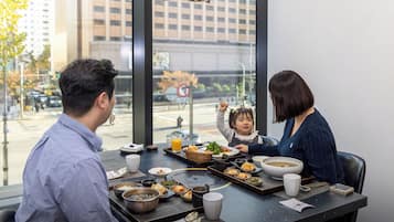 Una mesa de comedor con diferentes platos, vista a la ciudad por una ventana, y una persona levantando la mano.