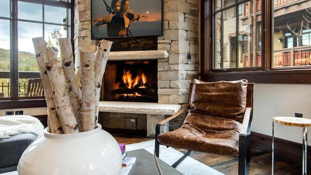 Een gezellige woonkamer met een stenen open haard, een comfortabele leren fauteuil en een grote televisie boven de open haard.