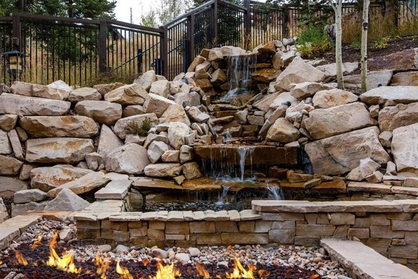 A stone waterfall feature with a fire pit in the foreground.
