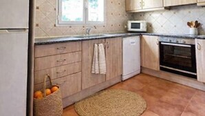 A kitchen with wooden cabinets, a microwave, a dishwasher, and a tiled floor. - Villa Fina (Ciutadella de Menorca)