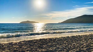 A beach with waves, a clear sky, and distant landforms.