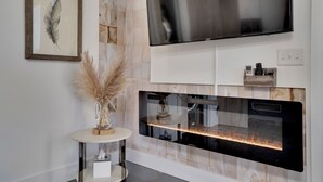 Uma sala de estar moderna com uma grande televisão de tela plana na parede, uma lareira embutida e uma obra de arte com penas emoldurada na parede.