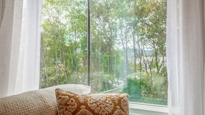 Una habitación con un ventanal grande, un cojín y cortinas traslúcidas.