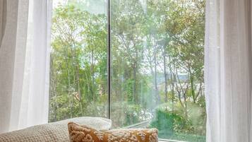 A room with a large window, a cushion, and sheer curtains.