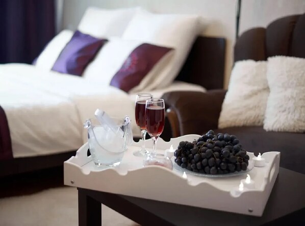 A tray with a bottle of champagne, two glasses of red wine, and a bowl of grapes on a table in a hotel room. - PaulMarie Apartments on Mira 25B (Mahilyow)