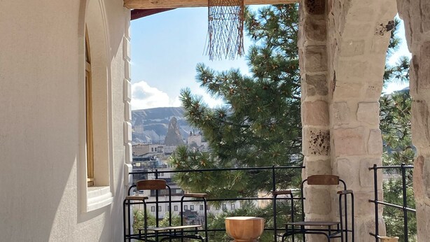 A balcony with a wooden ceiling, stone walls, and a view of mountains. There are metal chairs and a wooden table.