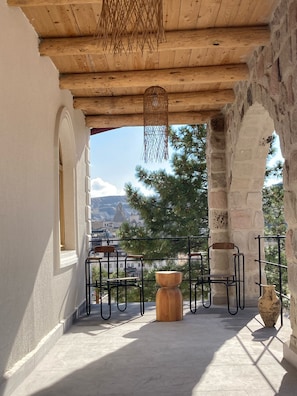 A balcony with a wooden ceiling, stone walls, and a view of mountains. There are metal chairs and a wooden table. - Naif Hotel - Adults Only (Nevsehir)