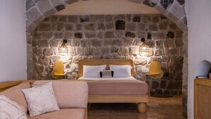 A cozy bedroom with a stone wall, a wooden bed, a wooden nightstand, and a pink sofa.