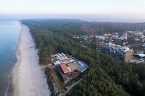 An aerial view of a coastal area with a beach, forested hills, and a mix of residential and commercial buildings.
