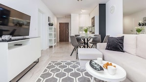 A modern living room with a sofa, coffee table, TV, and dining area.
