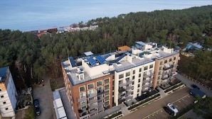 A multi-story building with balconies, a parking area, and a view of the sea.