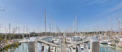 Una marina amb nombroses embarcacions amarrades, un pont per a vianants i un cel serè.