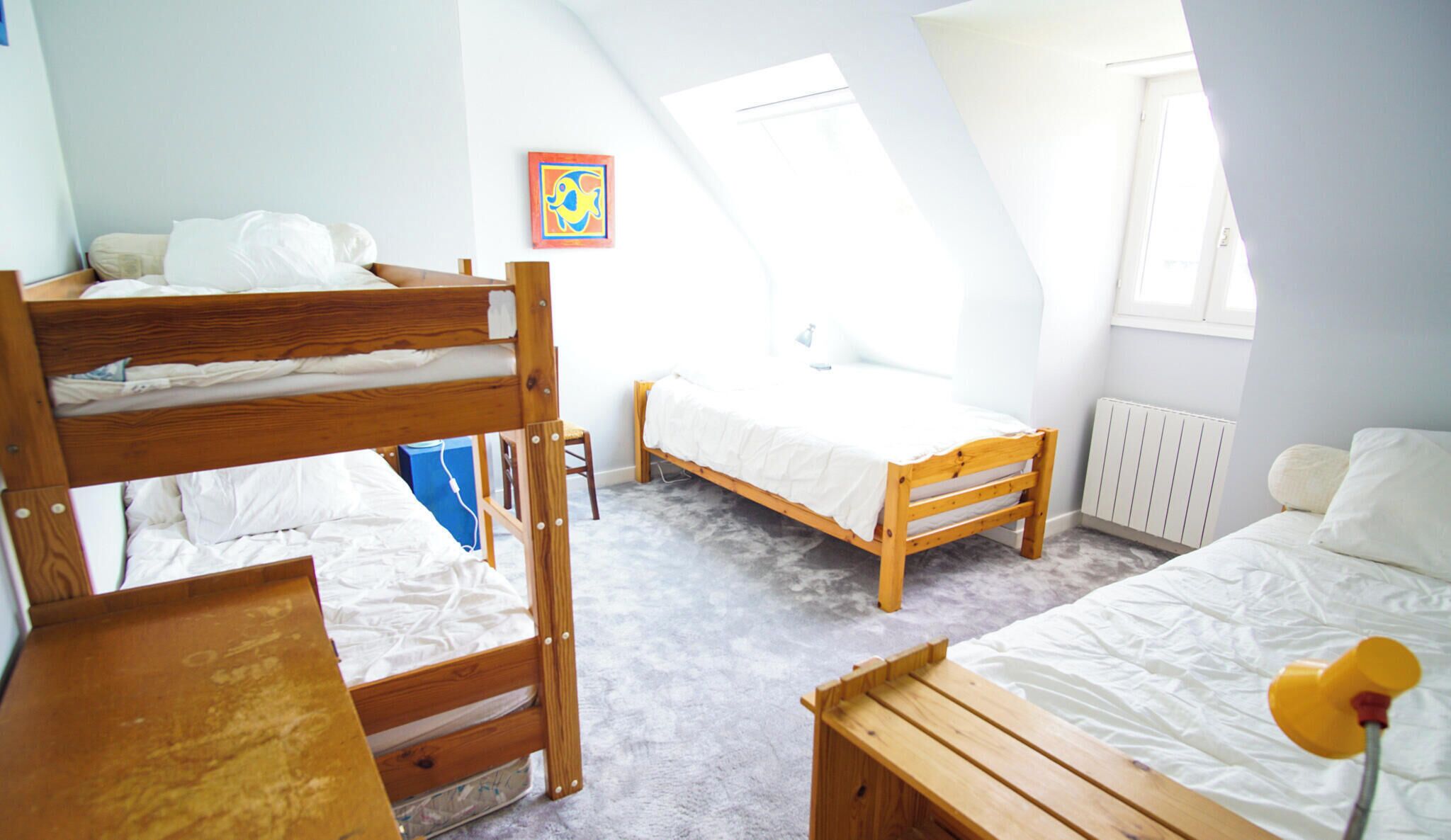 A dorm-style room with bunk beds, a single bed, a desk, and a radiator.